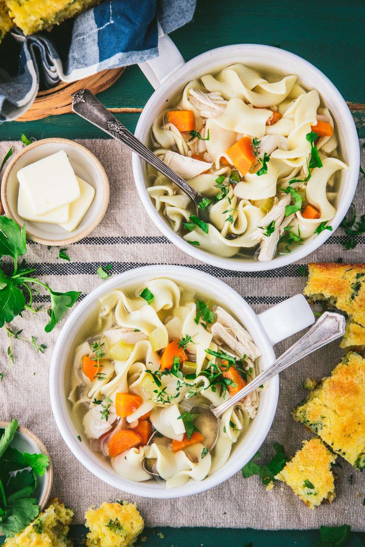 Two bowls of slow cooker chicken noodle soup on a table with cornbread