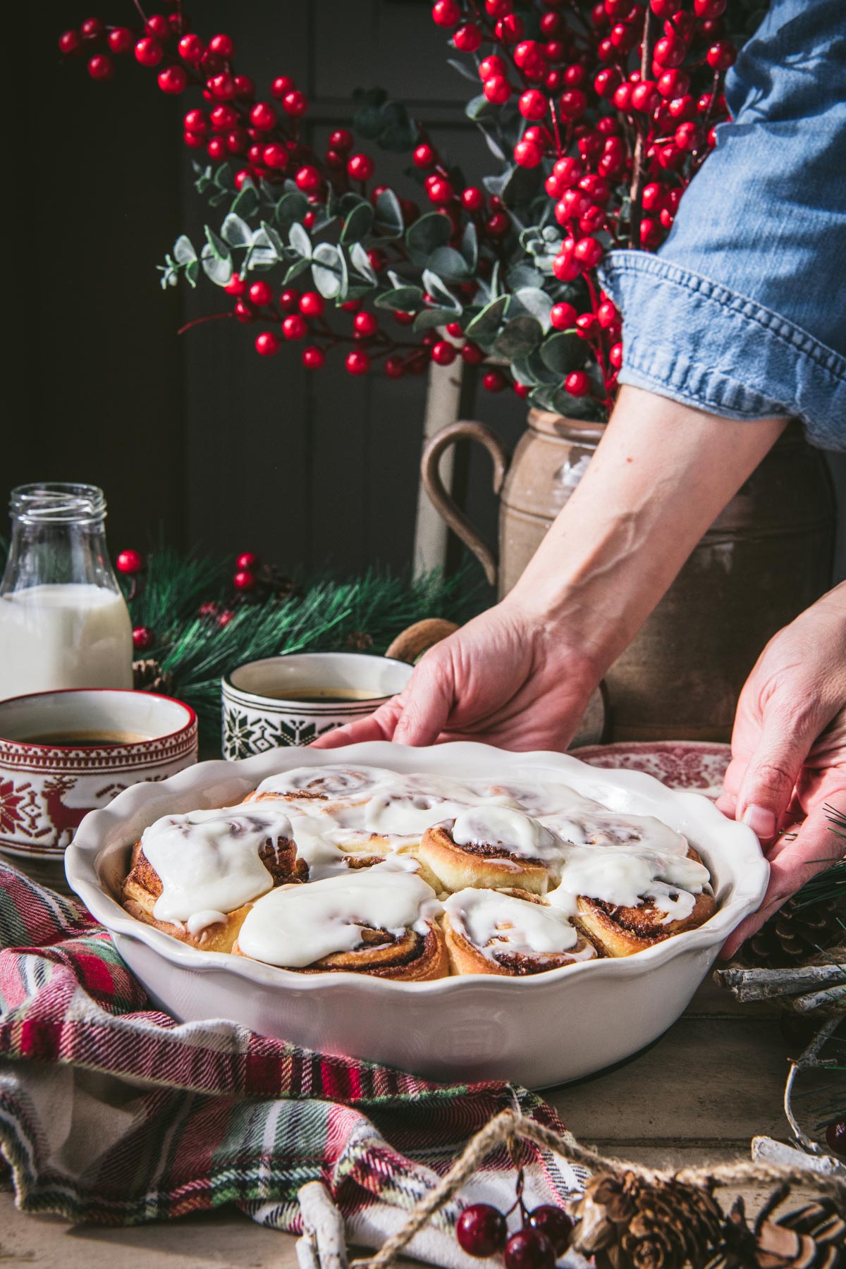 Hands serving a pan of cinnamon rolls on a Christmas table