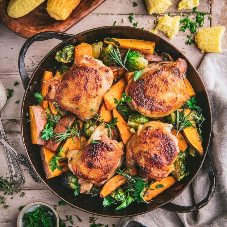 Square overhead shot of maple roasted chicken thighs with vegetables in a cast iron skillet on a wooden table