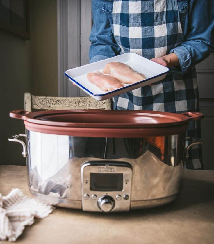 Placing chicken breasts into a slow cooker.