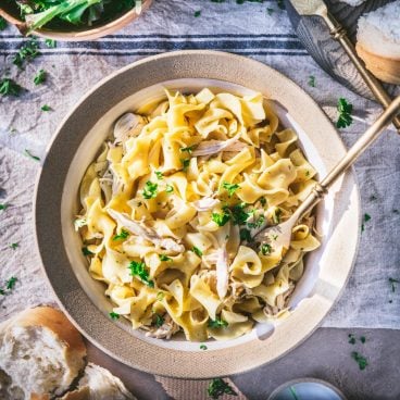 Square overhead image of crock pot chicken and noodles on a table.