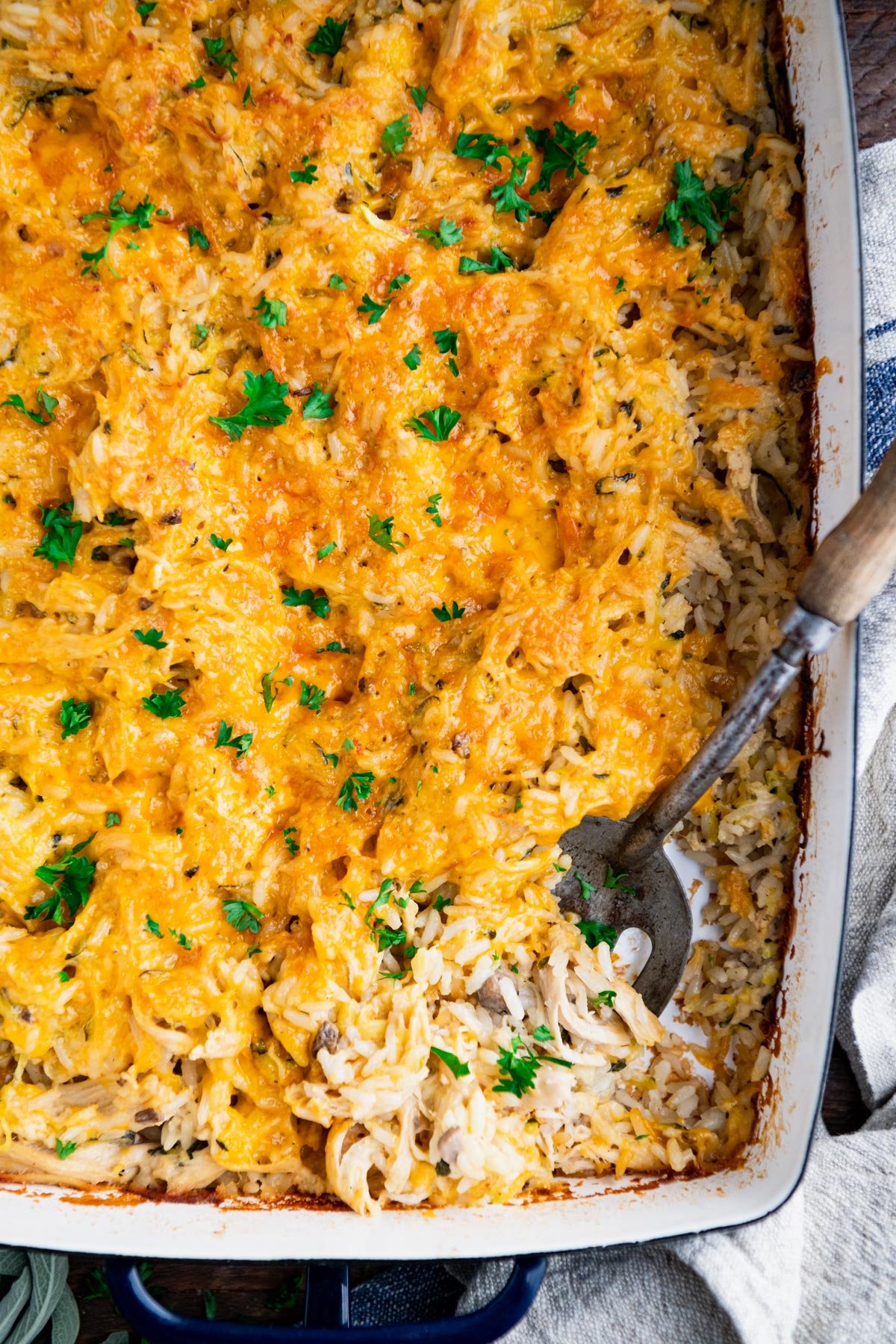 Close overhead shot of a serving spoon in a pan of cheesy chicken and rice casserole.