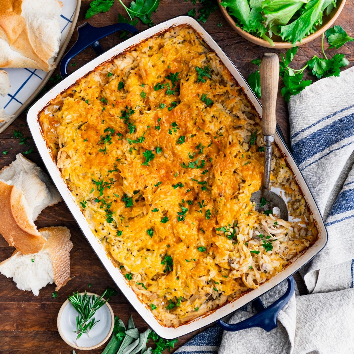 Square overhead image of cheesy chicken and rice casserole in a blue baking dish.