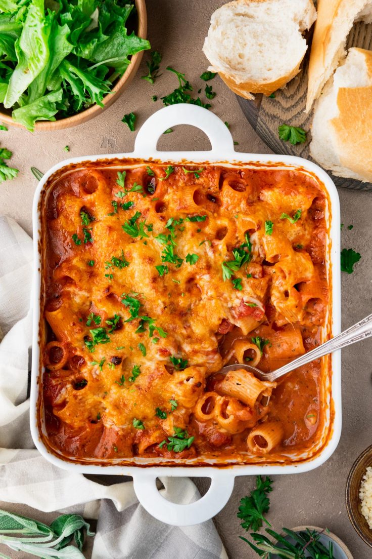 White casserole dish full of baked creamy tomato basil pasta with fresh herbs on top.