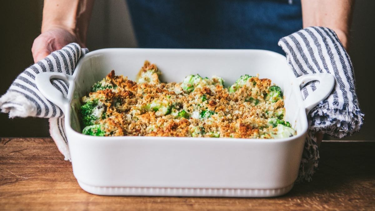 Square side shot of hands serving a dish of easy broccoli casserole
