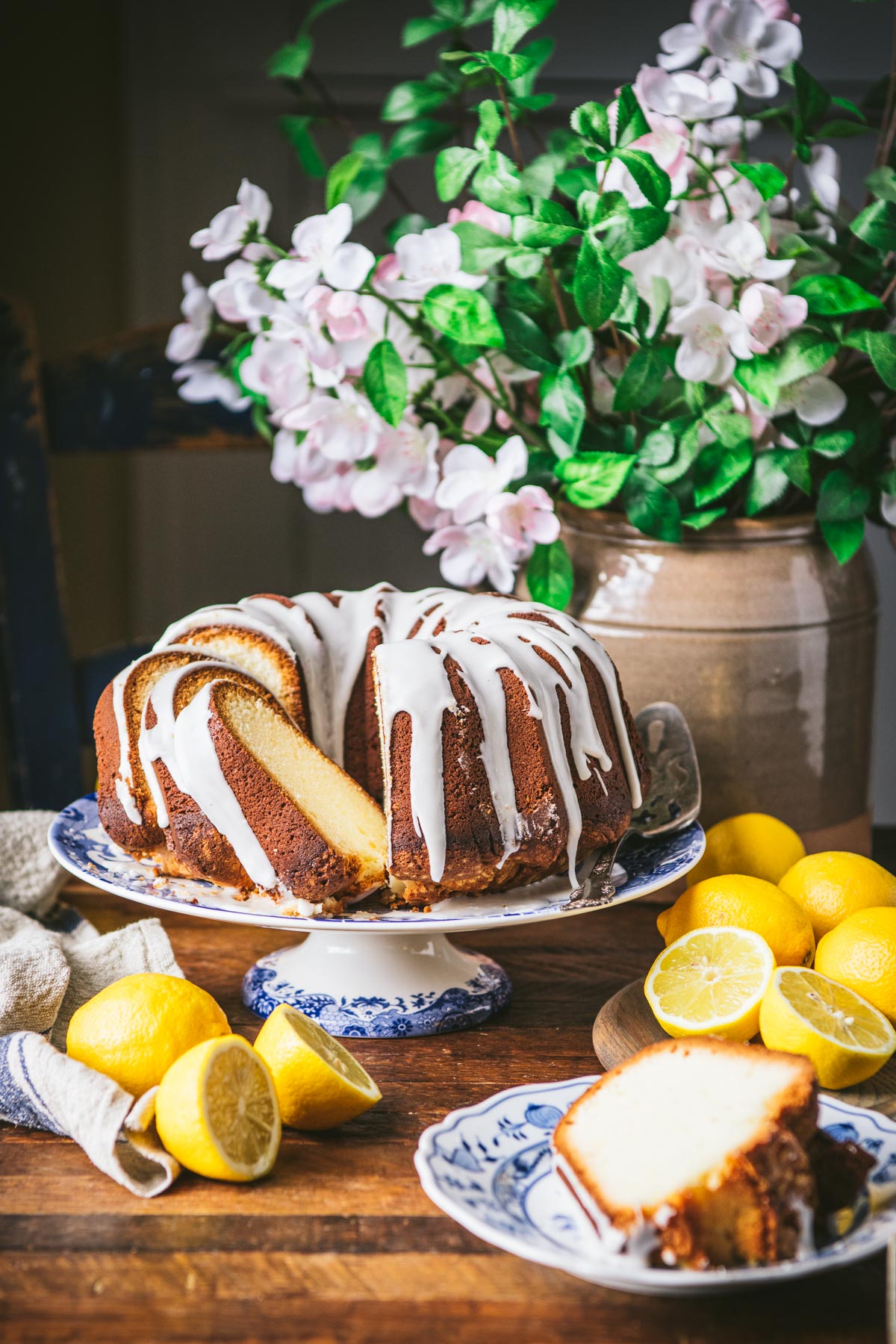 Side shot of lemon pound cake on a wooden table with flowers in the background.