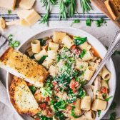 Overhead image of one pot chicken and spinach pasta in a bowl with a side of garlic bread.