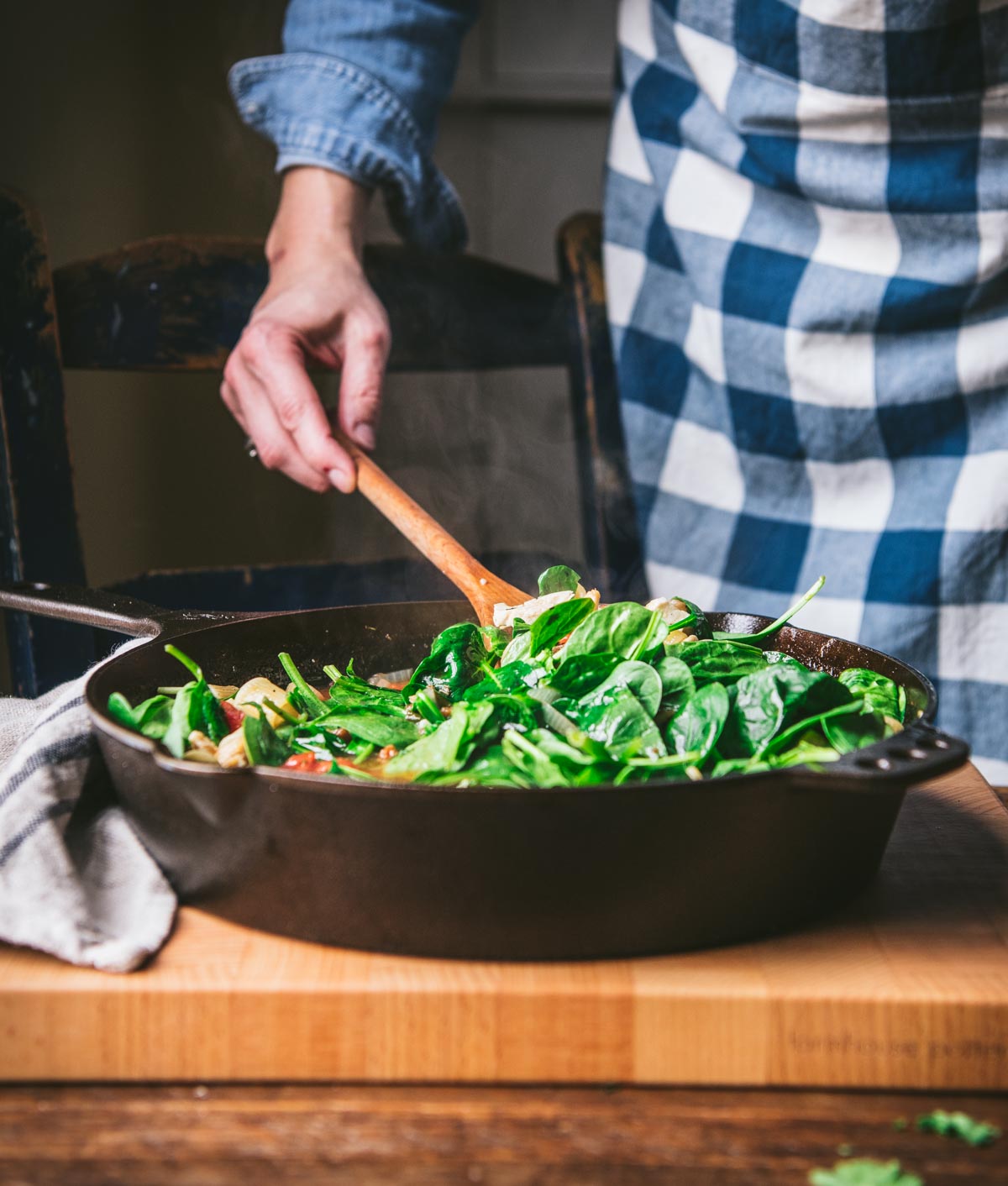 Stirring spinach leaves into a cast iron skillet with pasta.
