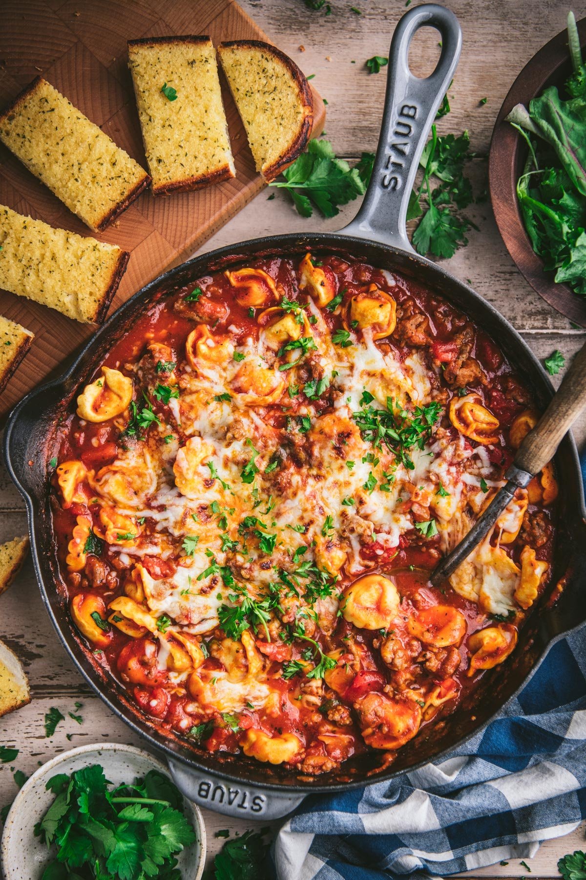 Overhead shot of a pan of sausage and cheese tortellini in marinara sauce with a side of garlic bread.