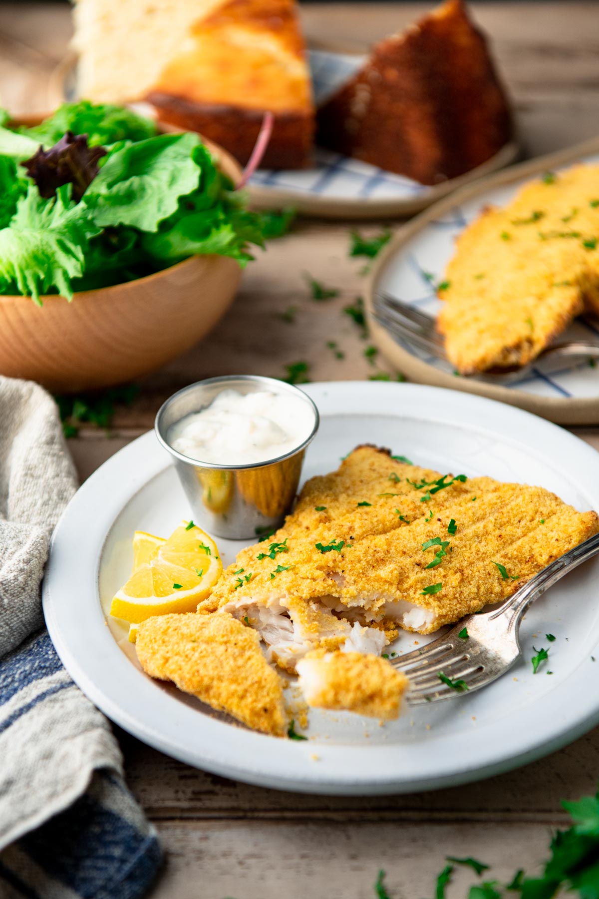 Front shot of a plate of baked catfish on a table with cornbread and salad.