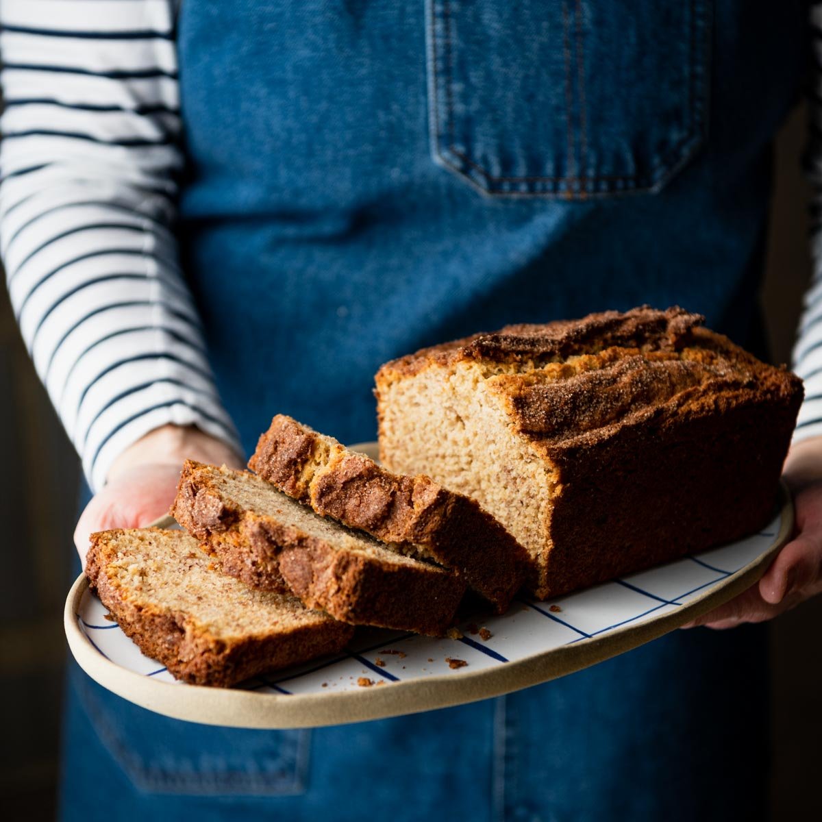Square side shot of hands holding a tray of buttermilk banana bread