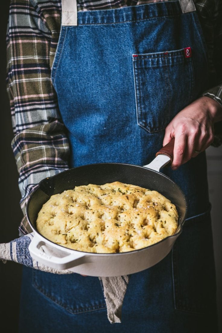Side shot of hands holding a skillet of cast iron focaccia.