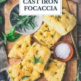 Slices of cast iron focaccia on a wooden board with text title overlay.