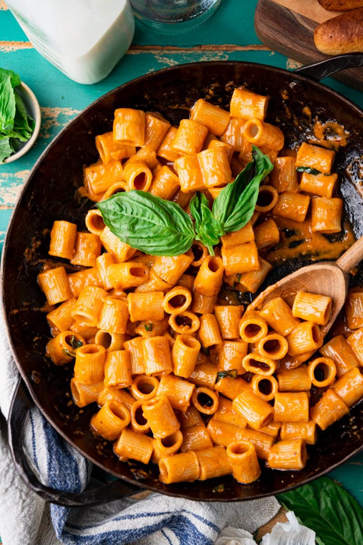 Wooden serving spoon in a pan of creamy tomato pasta sauce.