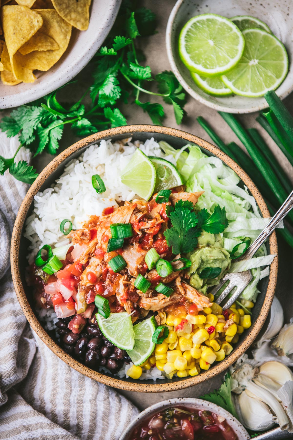 Overhead shot of crock pot chipotle chicken burrito bowl on a table with toppings.