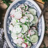 Creamy cucumber radish salad with dill on a blue and white platter.