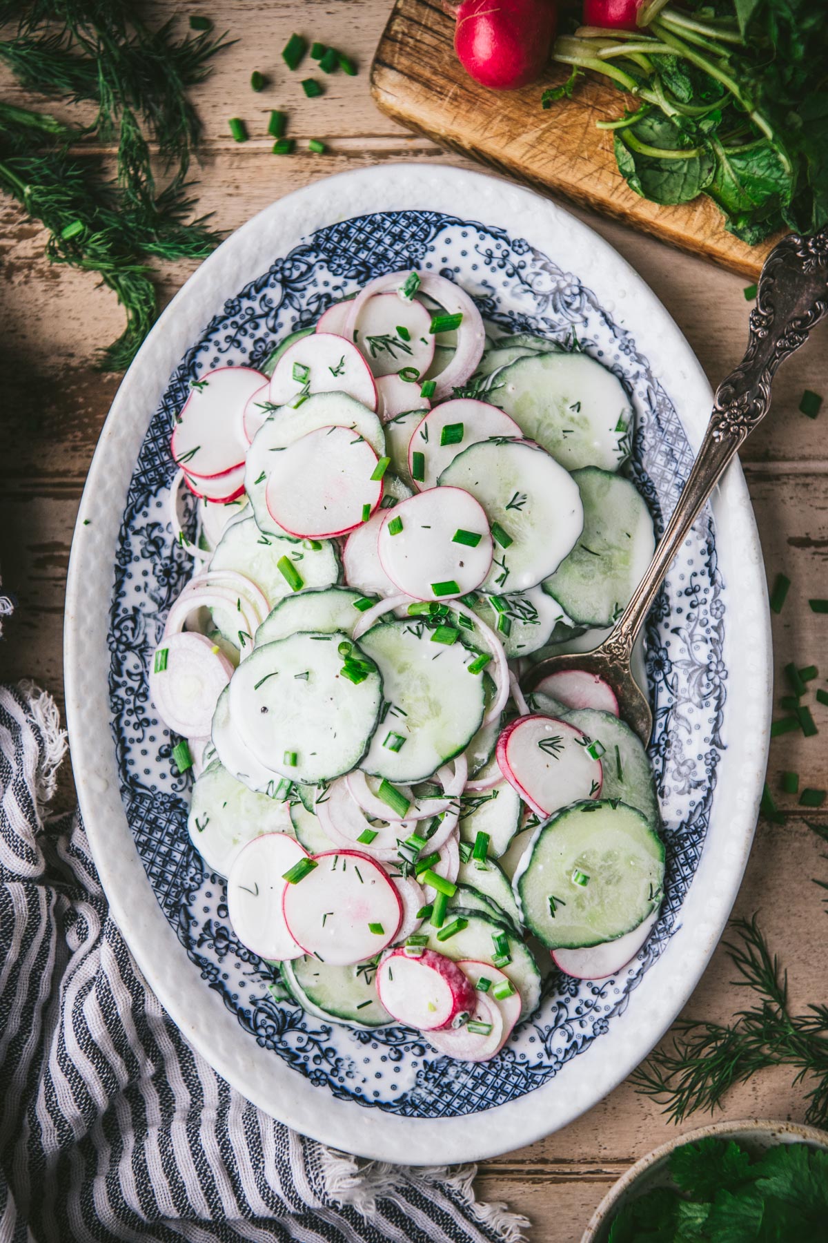 Creamy cucumber radish salad with dill on a blue and white platter.