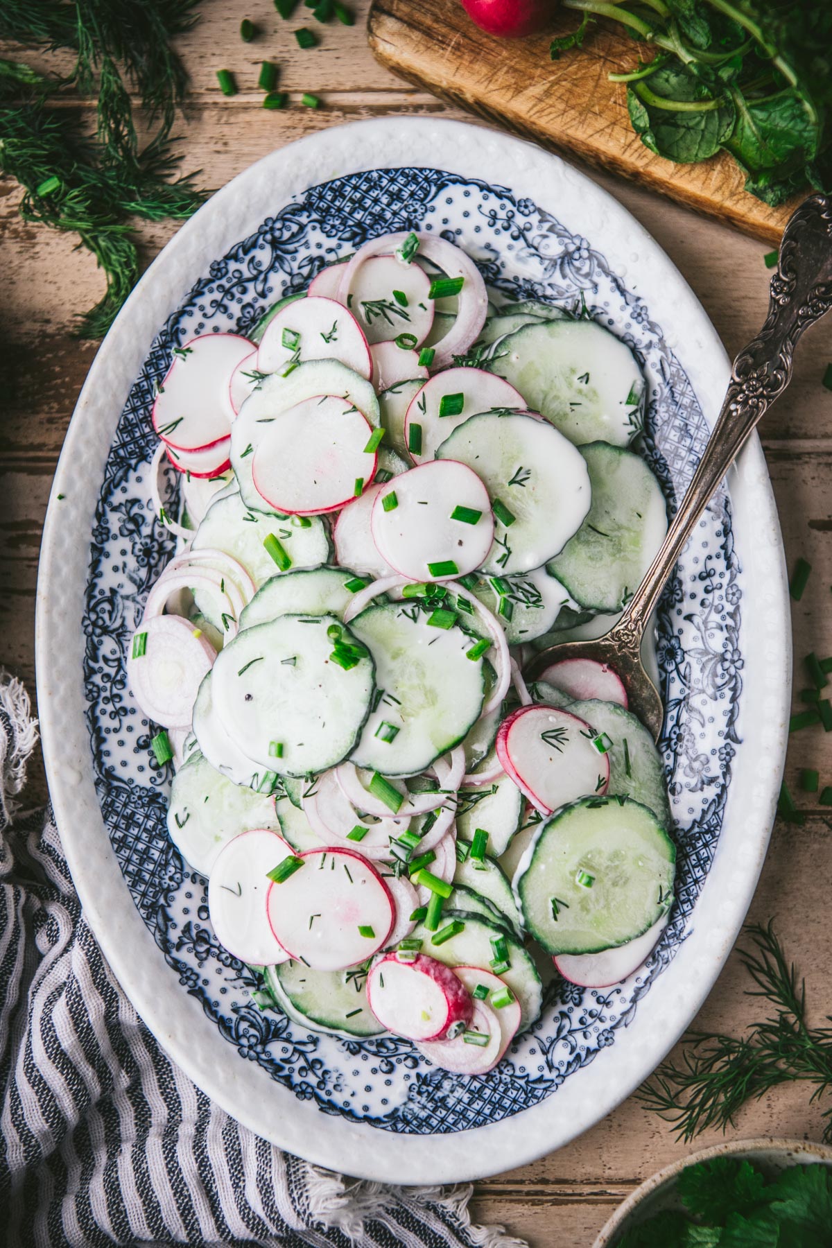 Vintage serving spoon on a blue and white plate full of cucumber radish salad.