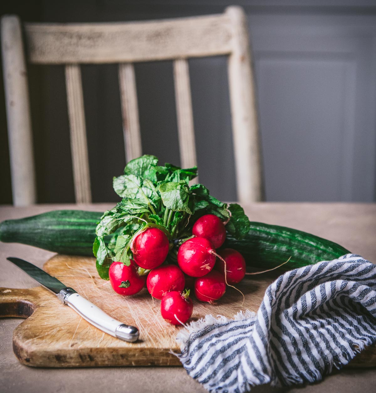 Cucumber and radishes on a vintage cutting board.