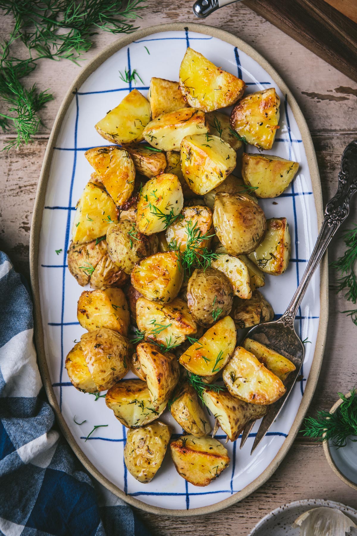 Serving spoon on a blue and white tray full of roasted potatoes with dill and lemon.