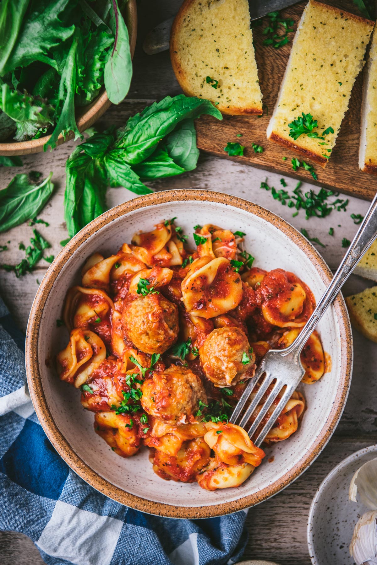 Overhead shot of a bowl of tortellini and meatballs with a side salad and garlic bread.