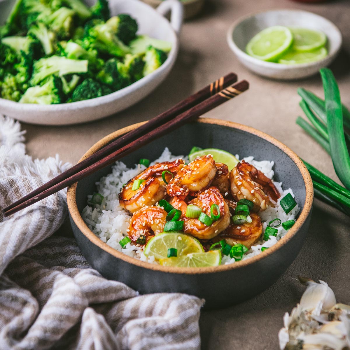 Square side shot of a honey sriracha shrimp rice bowl on a table with a side of broccoli