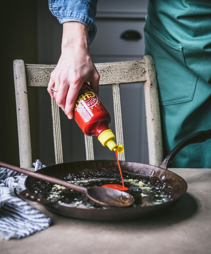 Process shot showing how to make honey sriracha shrimp in a skillet.