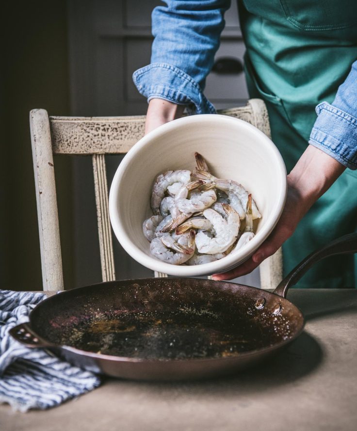 Adding shrimp to a cast iron skillet.