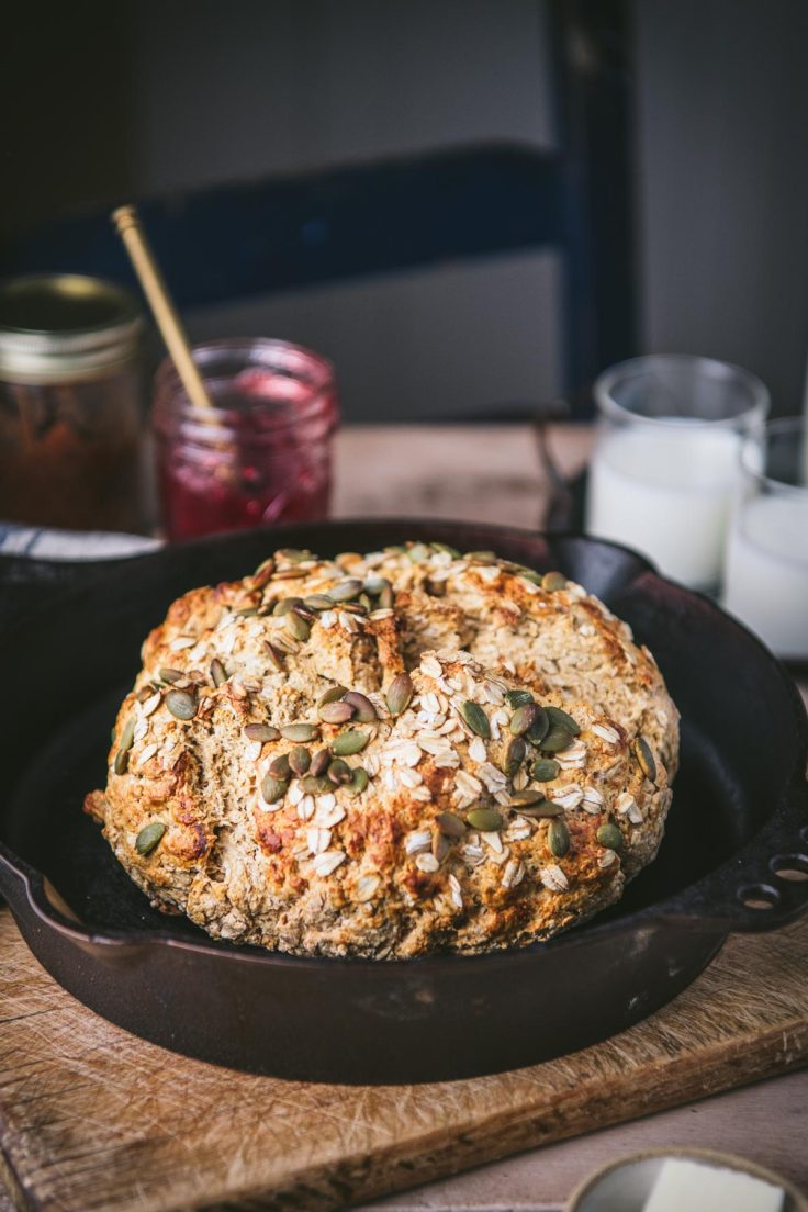 Baked loaf of soda bread in a cast iron skillet on a wooden table.