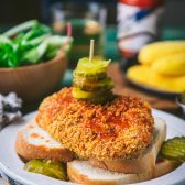 Side shot of a baked nashville hot chicken recipe served on a white plate with white bread and sliced pickles.