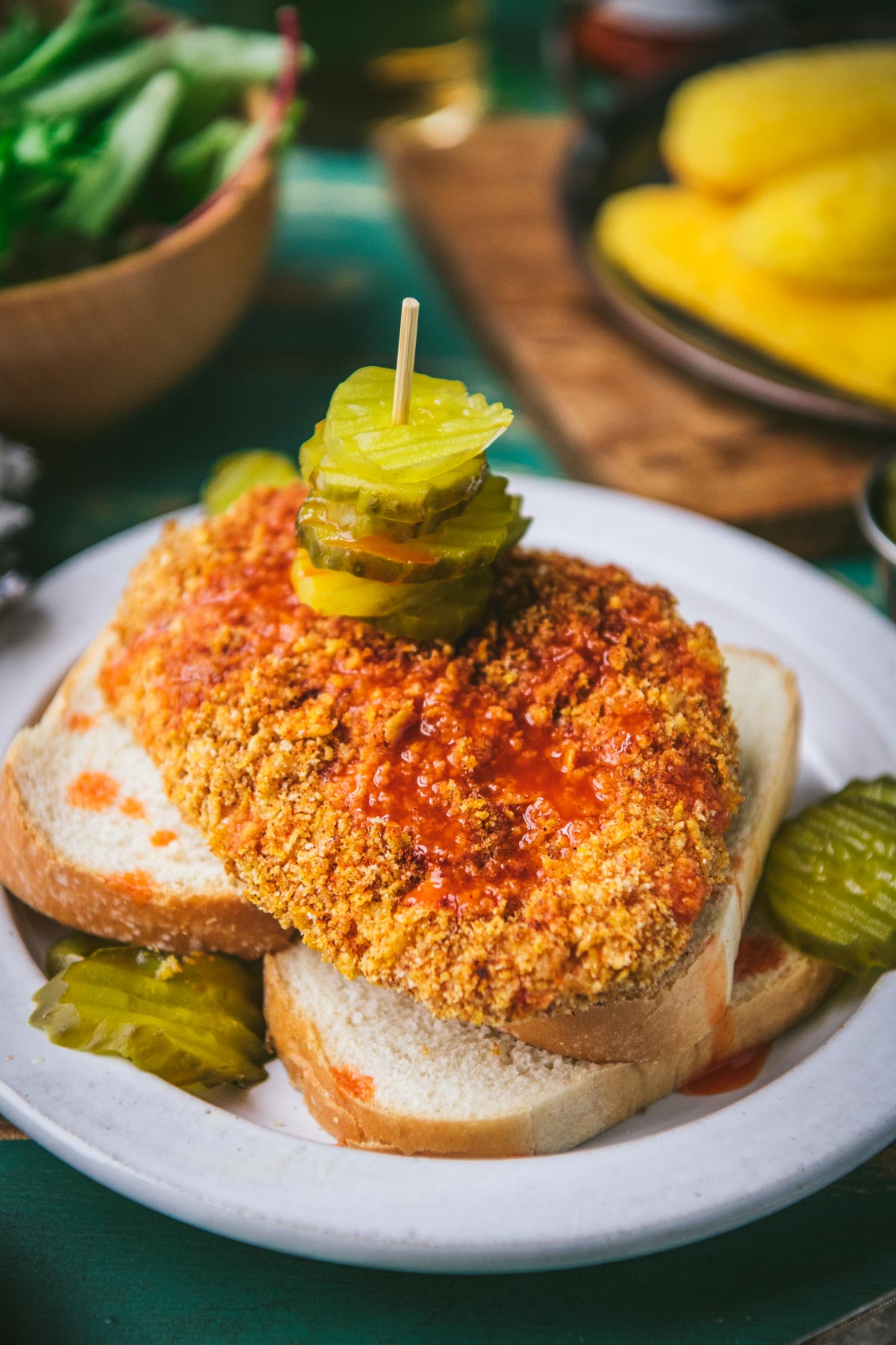 Close up front shot of baked nashville hot chicken recipe on a plate with bread and pickles.