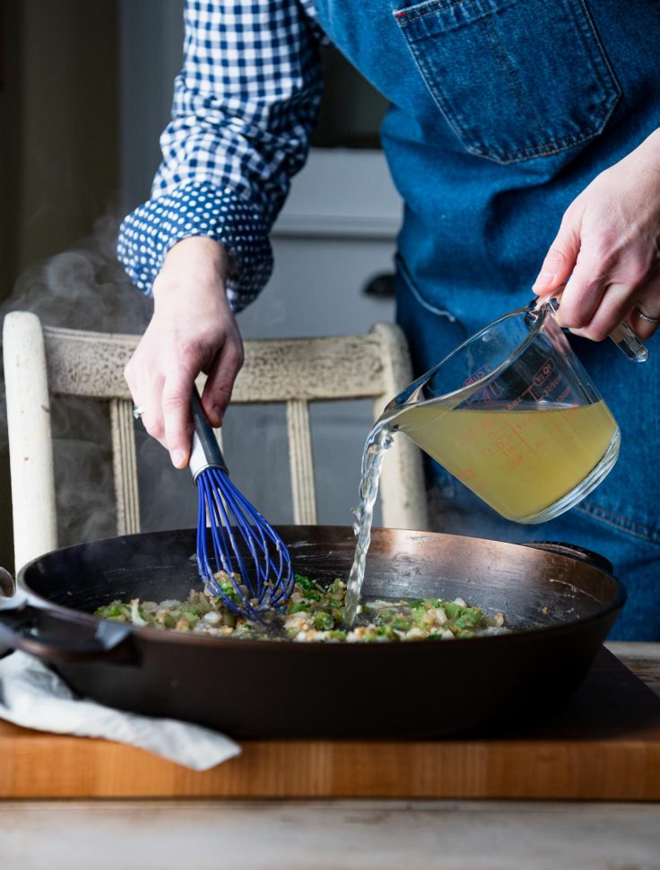 Pouring broth into a cast iron skillet.