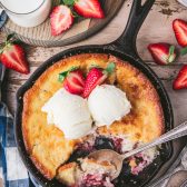 Overhead image of a cast iron skillet full of easy strawberry cobbler on a wooden table.
