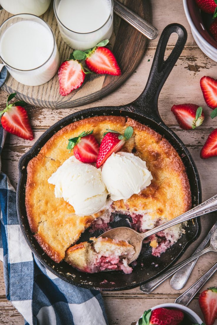 Overhead image of a cast iron skillet full of easy strawberry cobbler on a wooden table.