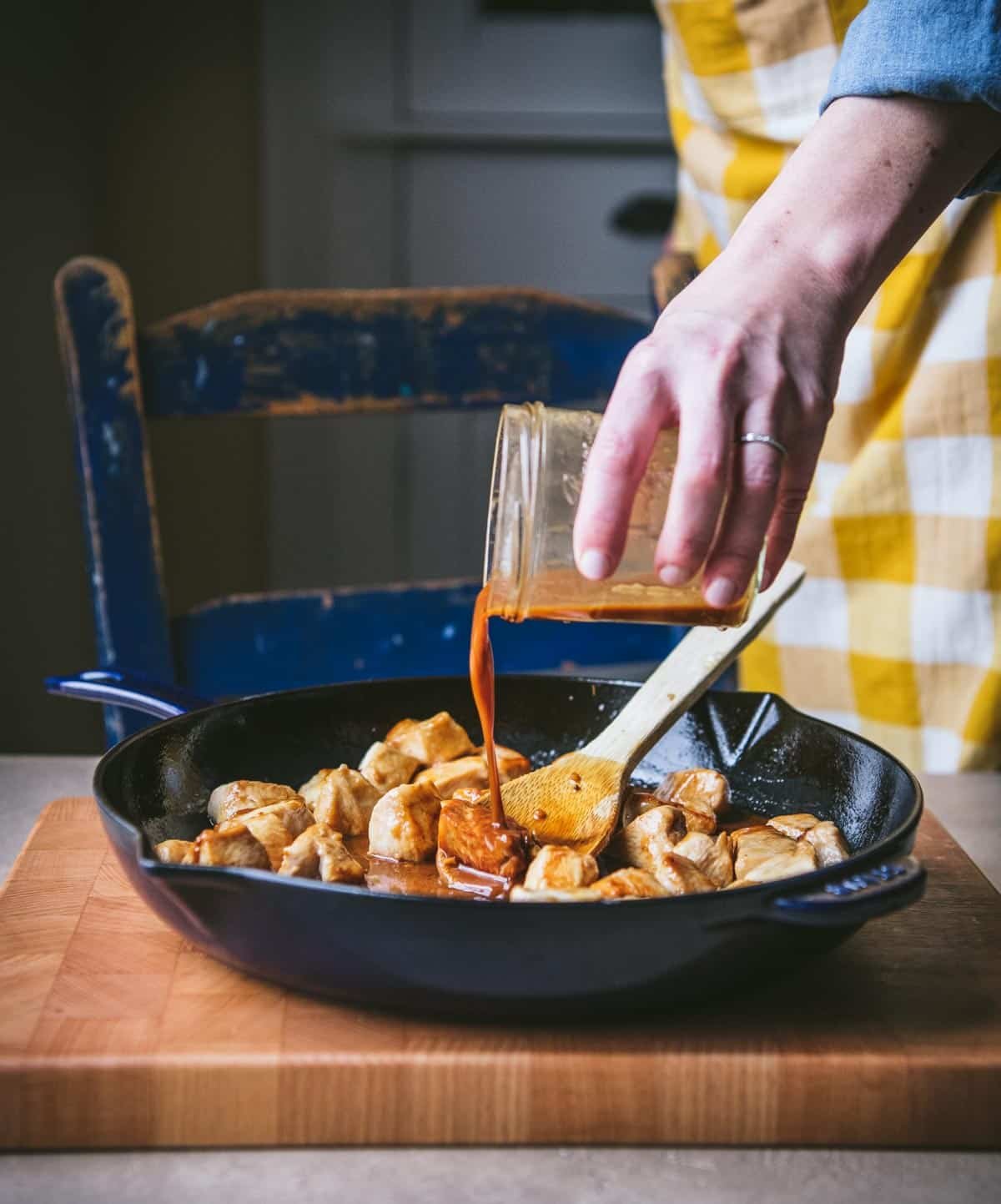 Pouring stir fry sauce into a skillet with chicken.