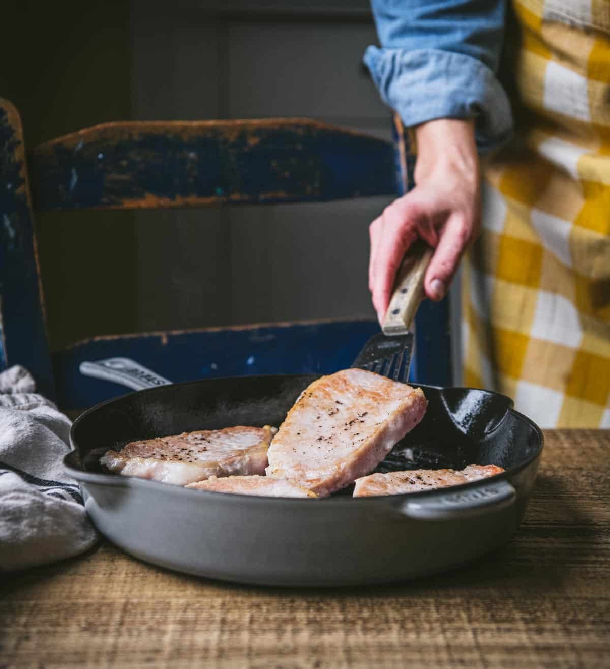 Pan frying pork chops in a cast iron skillet.