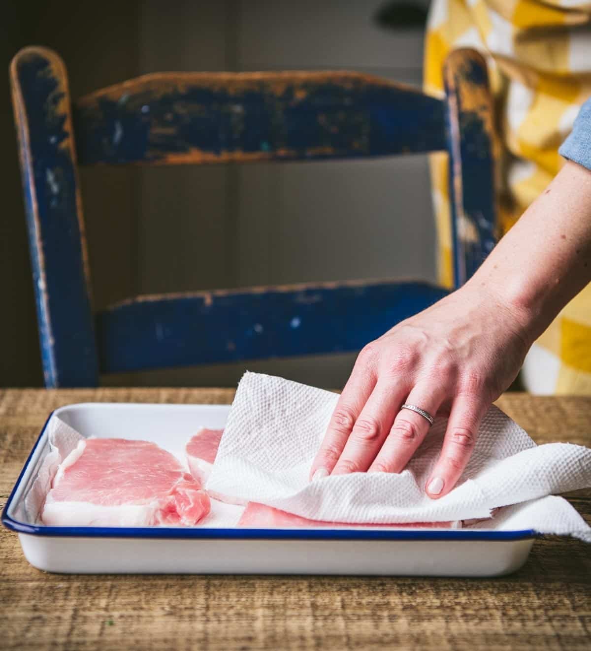 Patting pork chops dry with paper towels.