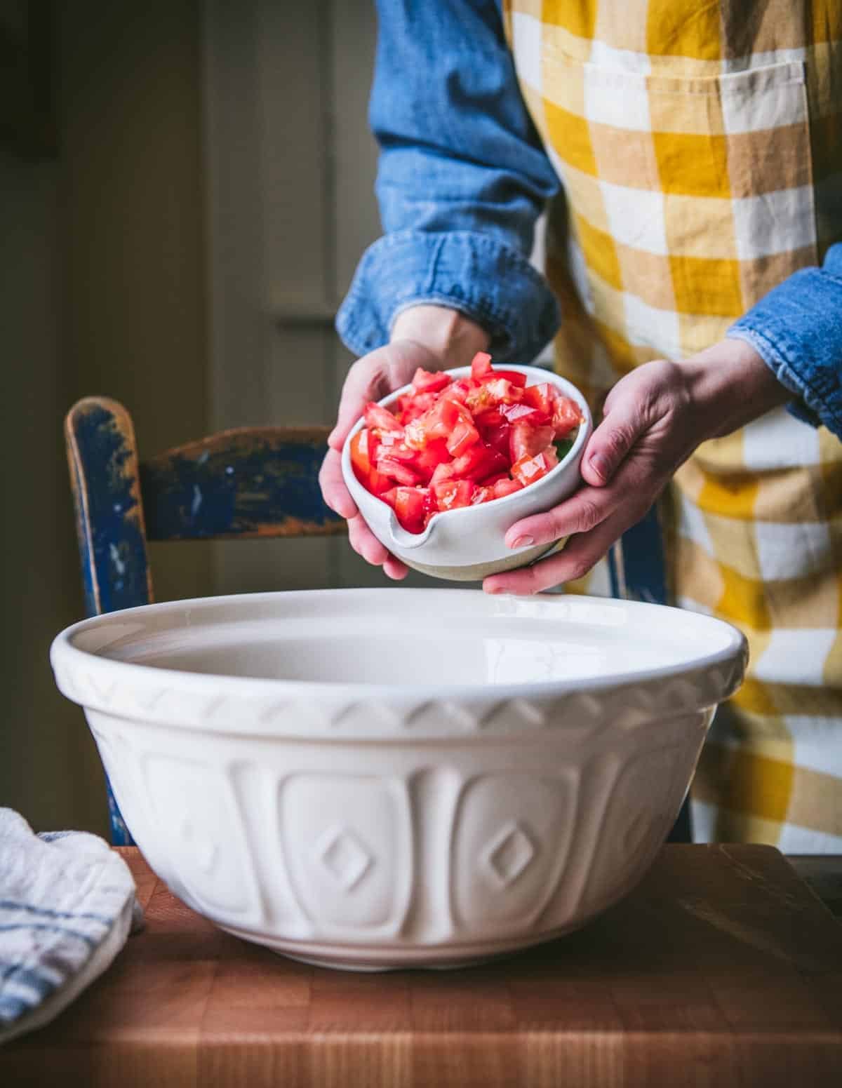 Adding tomatoes to a big white mixing bowl.