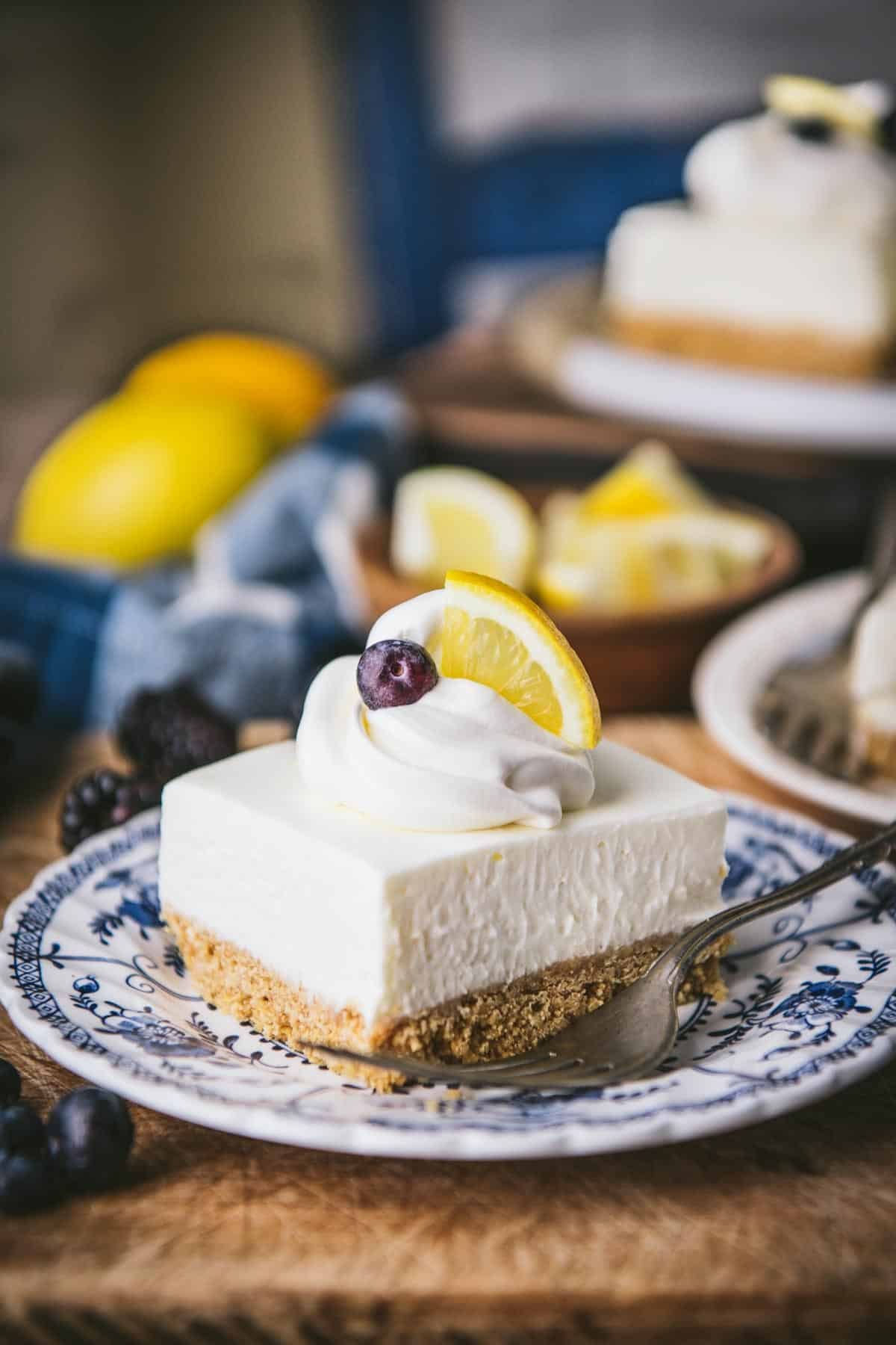 Side shot of lemon squares with graham cracker crust topped with lemon wedges and berries.
