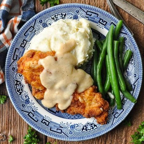 Overhead square shot of a plate of fried chicken cutlets with gravy and mashed potatoes.