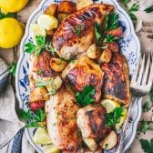 Overhead shot of sheet pan Greek chicken and potatoes with lemons and herbs on a tray.