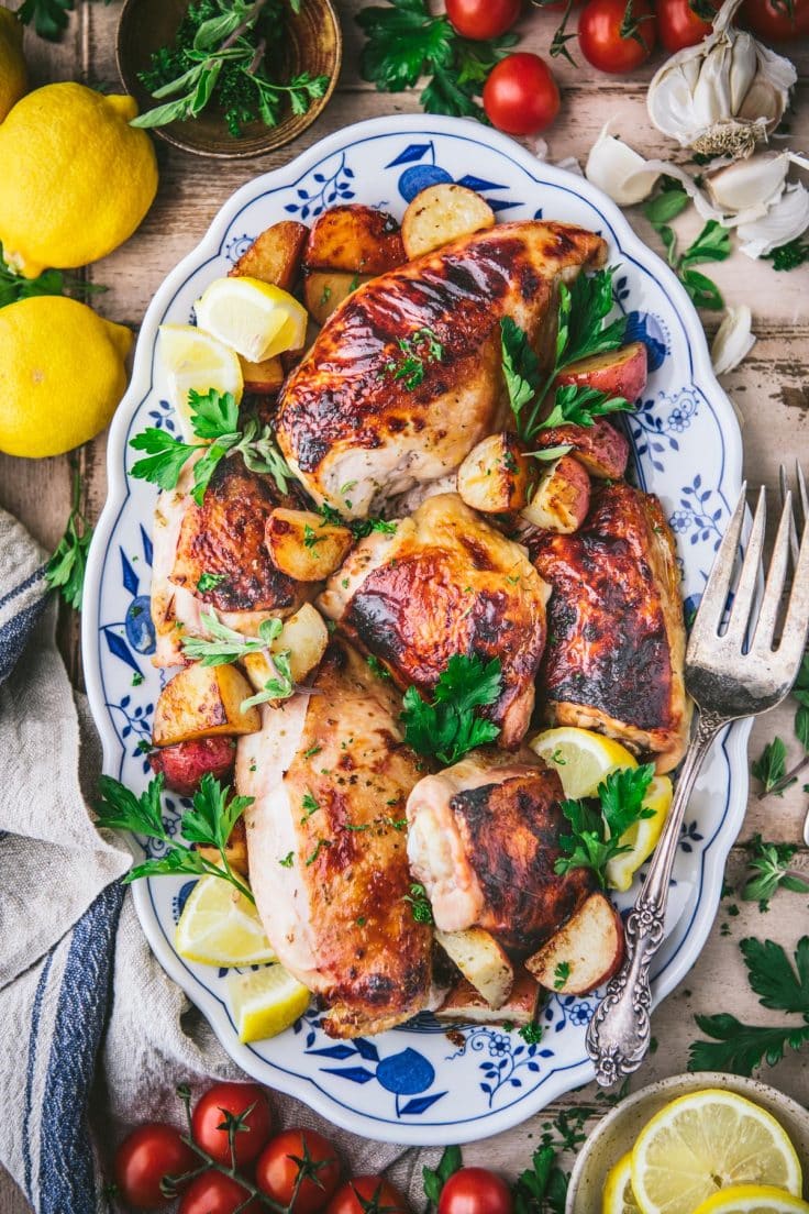 Overhead shot of sheet pan Greek chicken and potatoes with lemons and herbs on a tray.