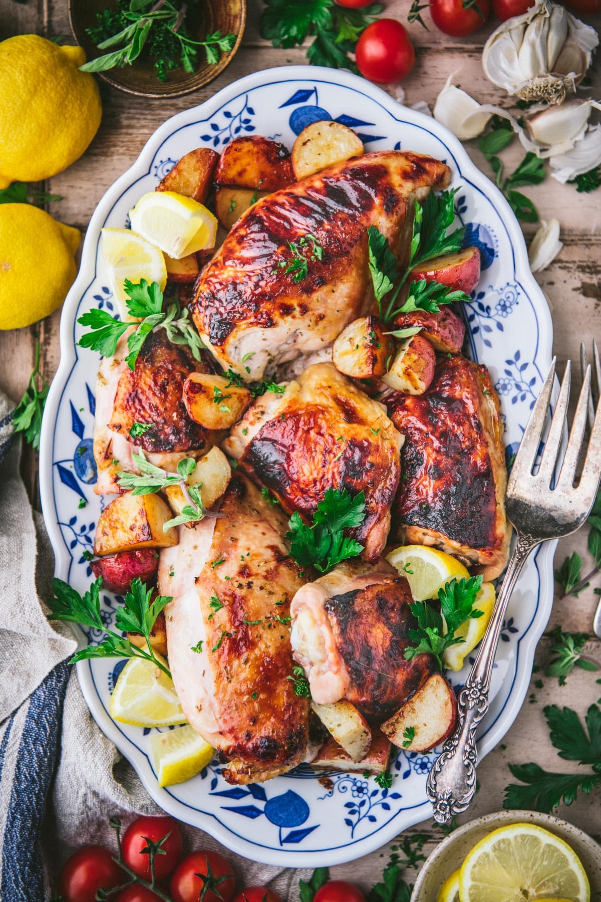 Overhead image of greek lemon chicken and potatoes with fresh herbs on a platter.