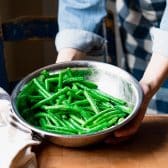 Green beans in a bowl with olive oil and seasoning.