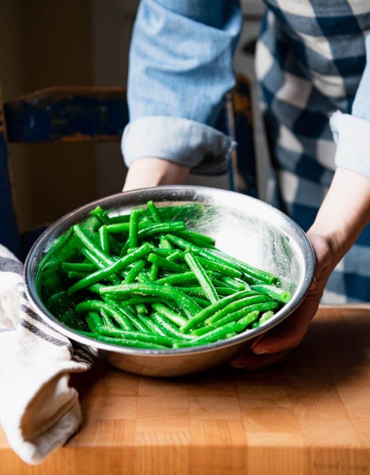 Green beans in a bowl with olive oil and seasoning.