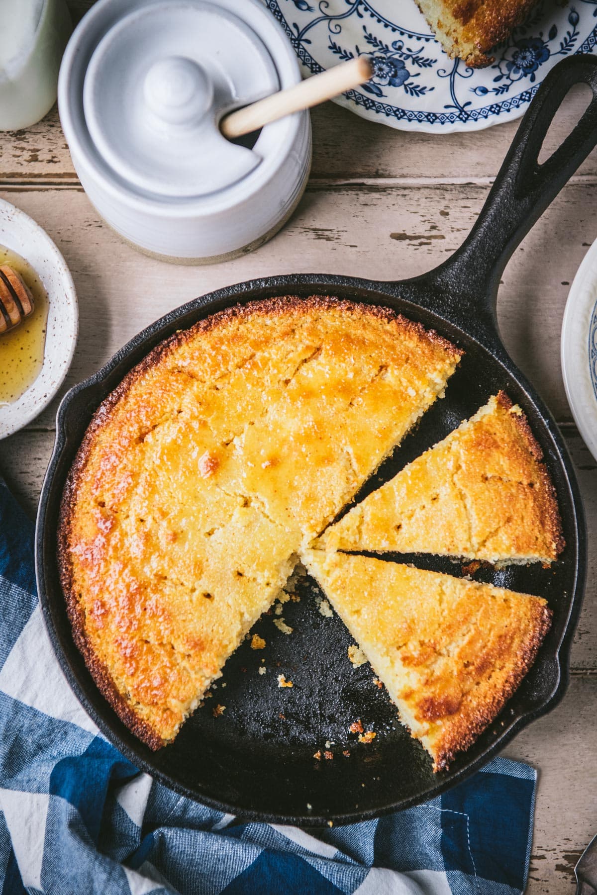 A skillet of sliced honey butter cornbread on a wooden table.