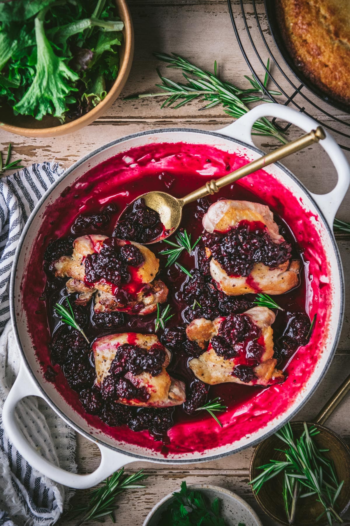 Overhead shot of a white cast iron skillet with chicken thighs and blackberry sauce.