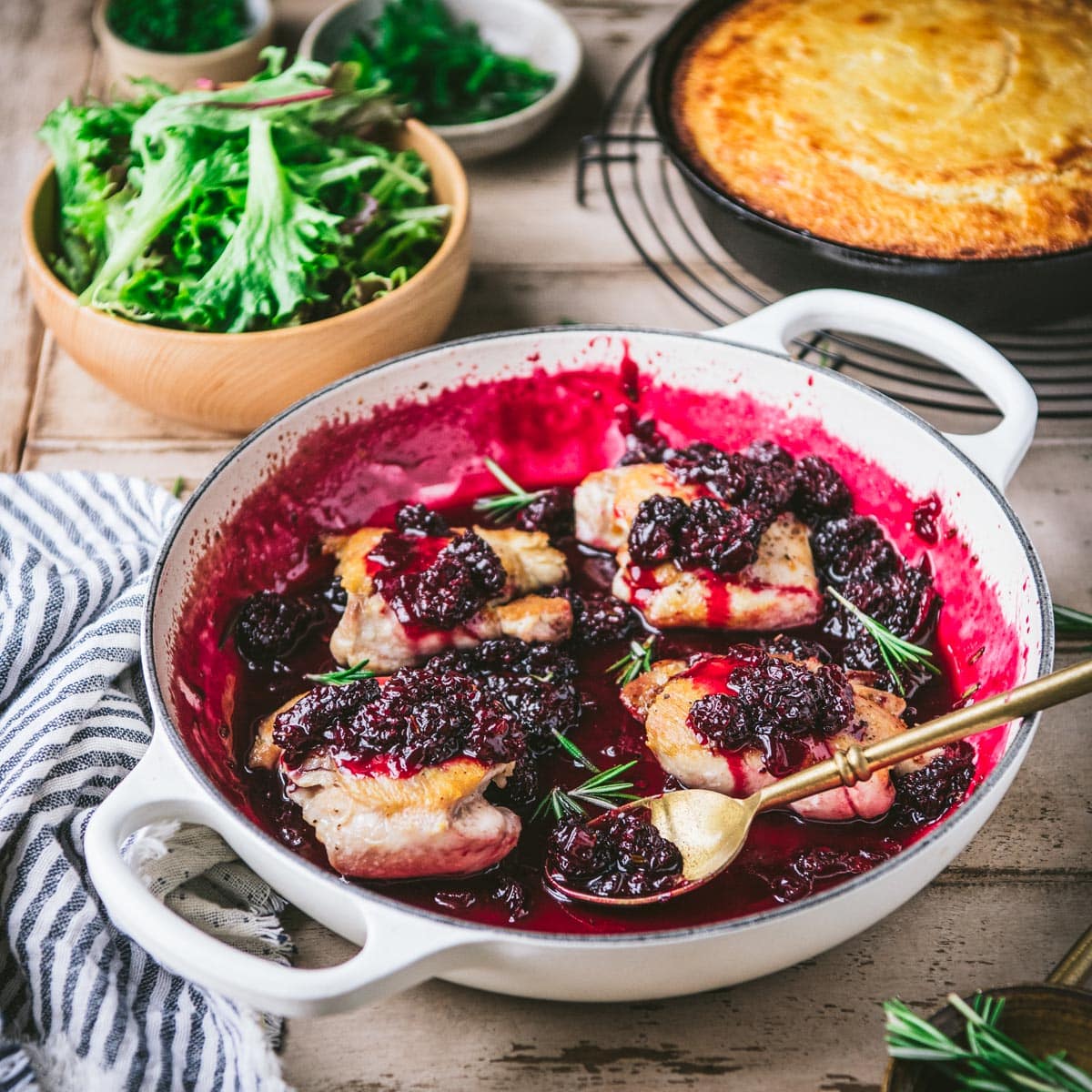 Blackberry chicken in a white cast iron skillet on a wooden dinner table.