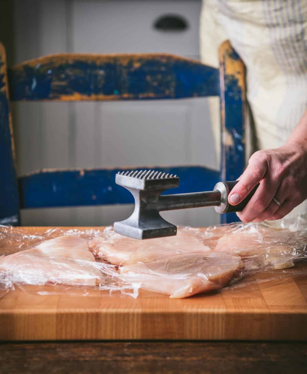 Pounding chicken breast flat with a meat mallet.