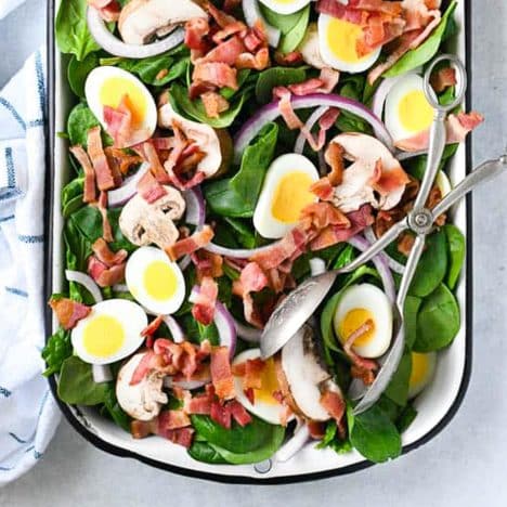 Square overhead shot of spinach salad with bacon and hardboiled eggs and poppy seed dressing